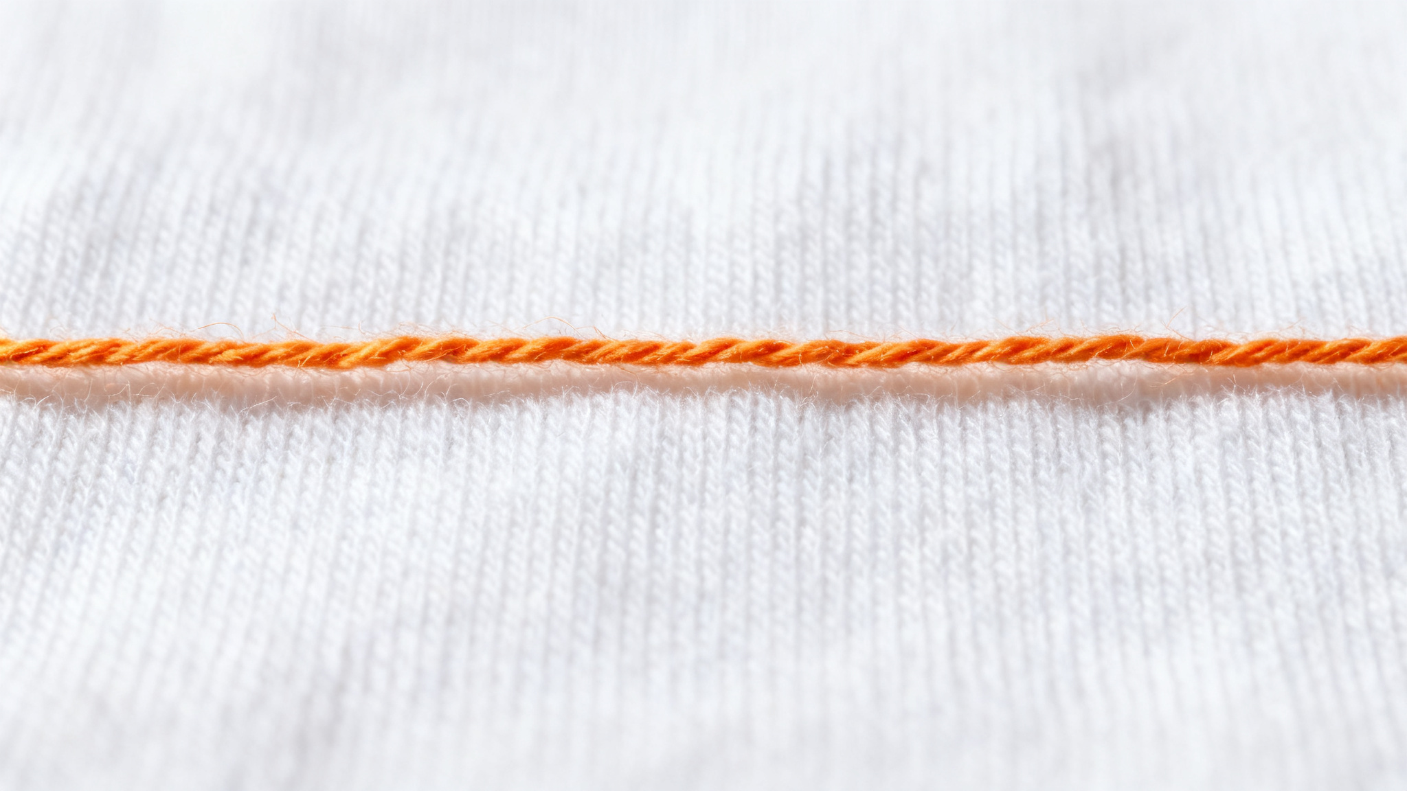 Macro close-up of pure white cotton jersey knit fabric showing loop structure and soft staple fibres with an orange thread
