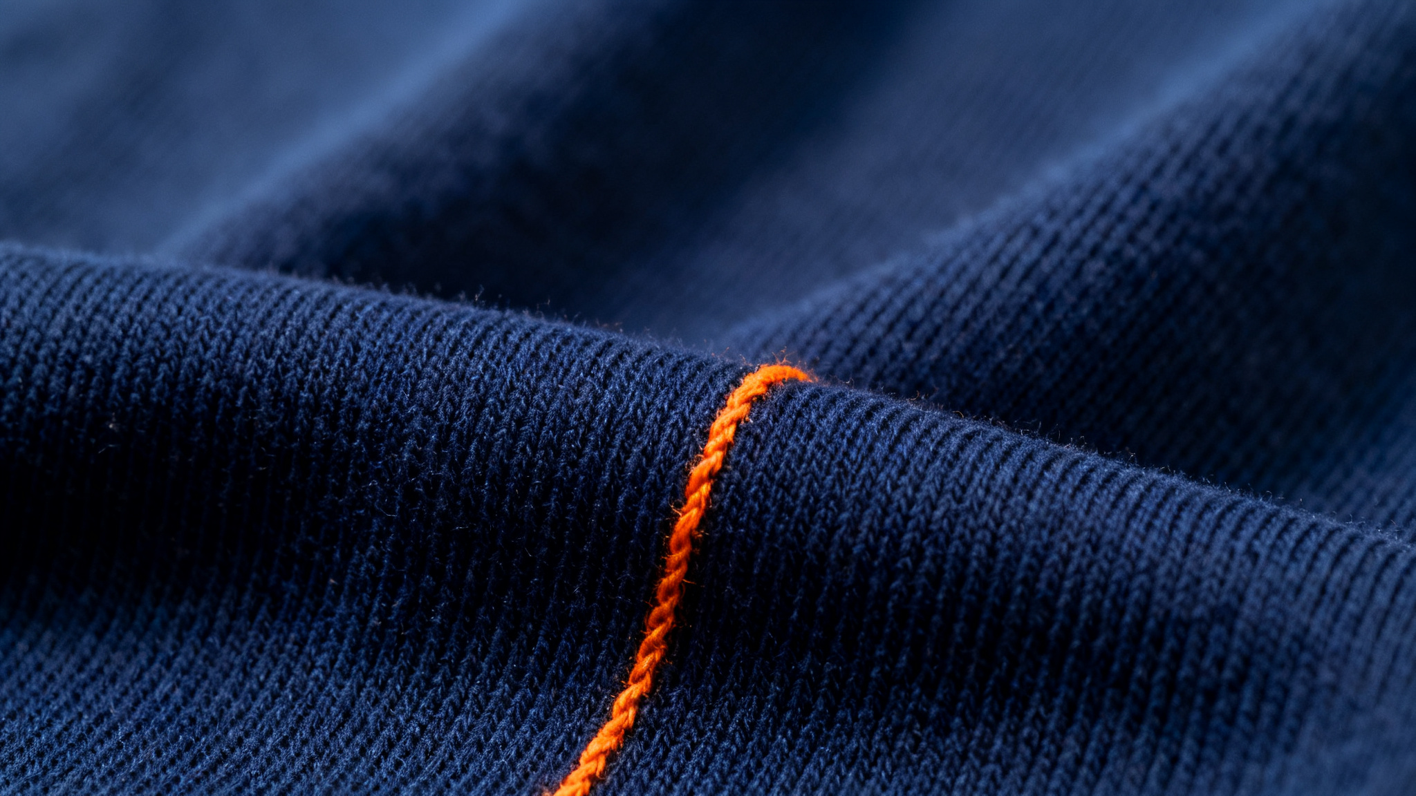 Macro close-up of premium cotton jersey knit fabric in deep navy blue with a warm orange thread